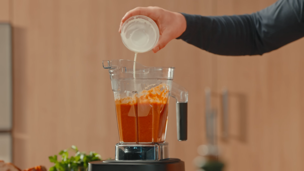 Heavy cream being poured into a blender of tomato soup.