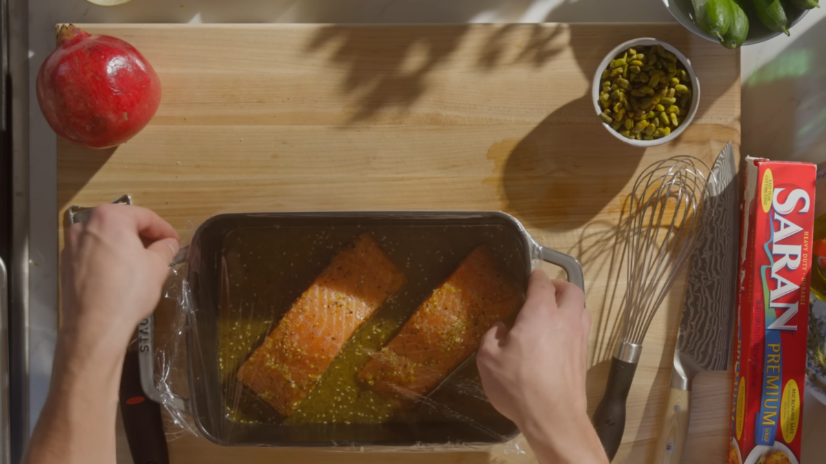 Salmon marinading in a metal baking dish covered with plastic wrap.