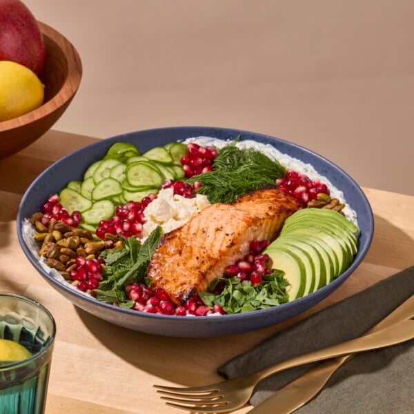 A farro grain bowl with salmon, cucumbers, avocado, feta, and pomegranate seeds.