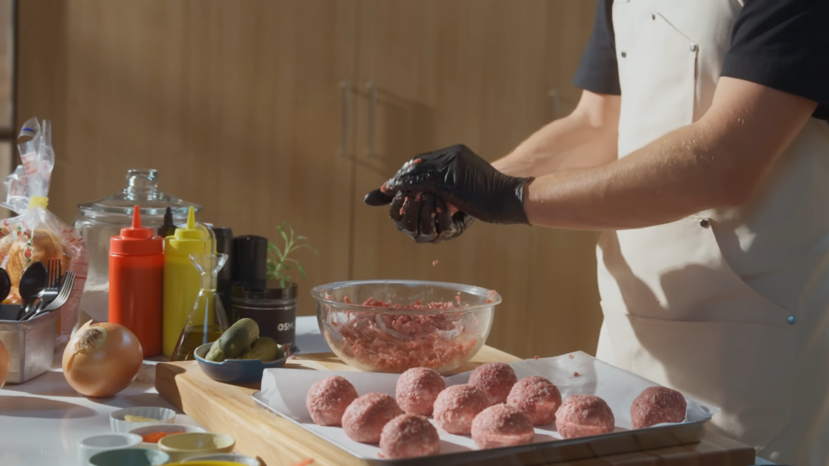 A man forming balls of ground beef and placing them on a metal sheet.