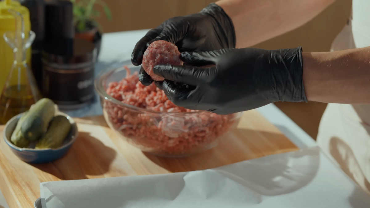 A man holding a ball of raw ground beef.