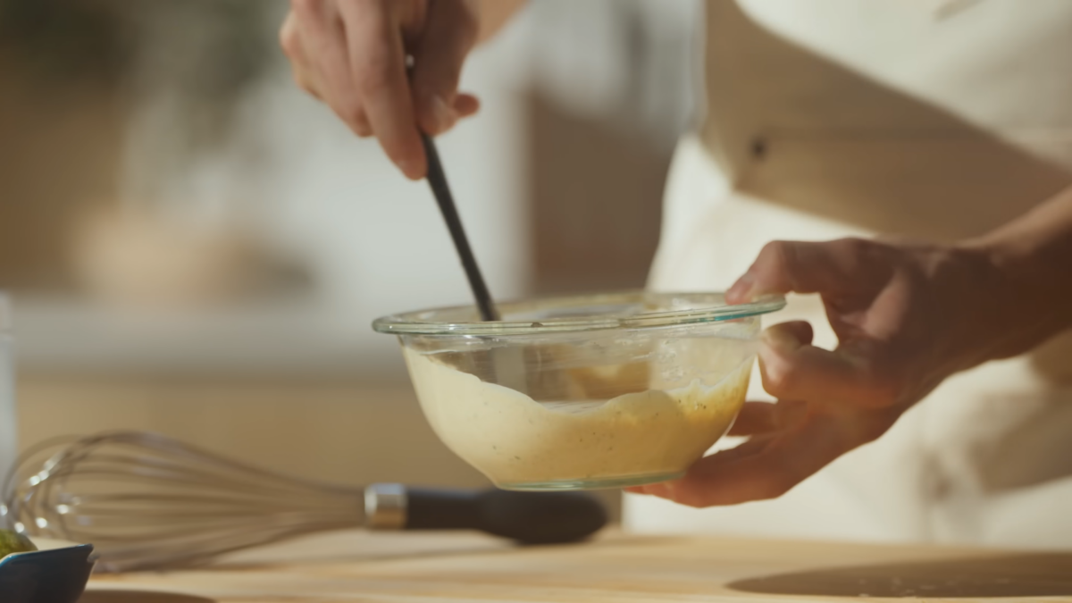 A man mixing sauce in a glass bowl.