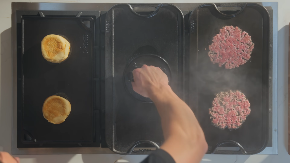 A man smashing burger patties on a cast iron griddle.