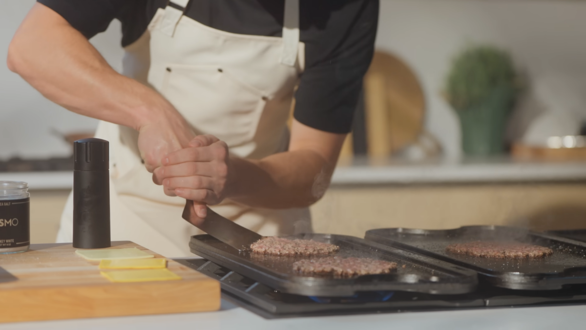 A man flipping burgers on a griddle.