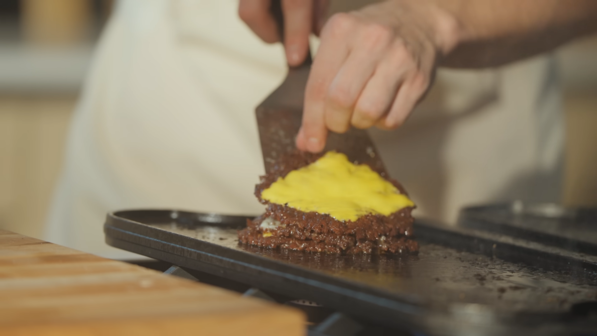 A male chef stacking burger patties.