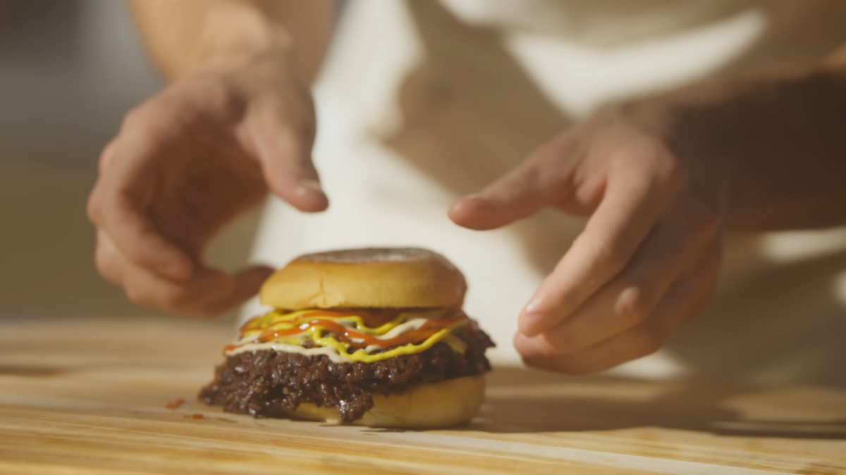 A layered smash burger topped with pickles and sauces.
