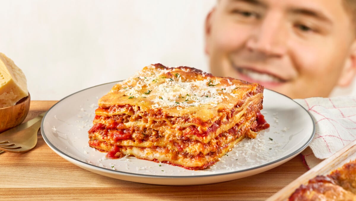 A man kneeling down next to a slice of lasagna on a plate.