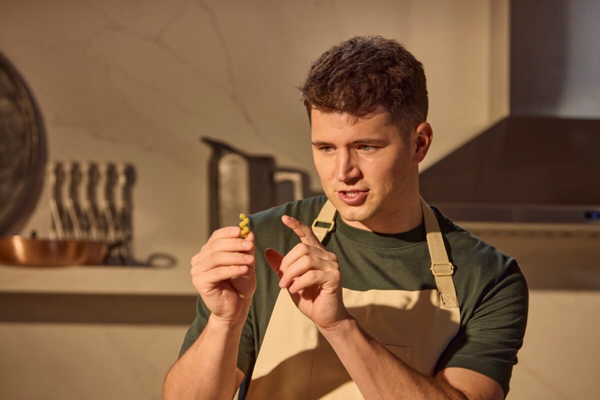 A male chef holding a cavatappi noodle pointing out the shape.
