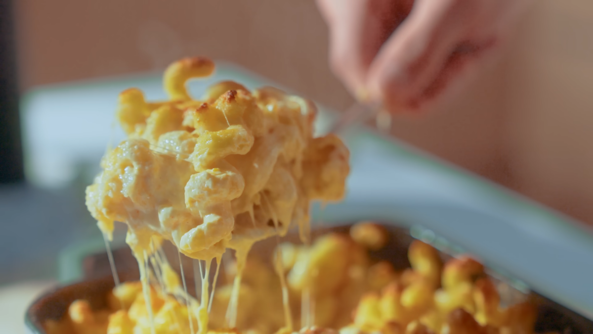 A man scooping stringy creamy mac and cheese.