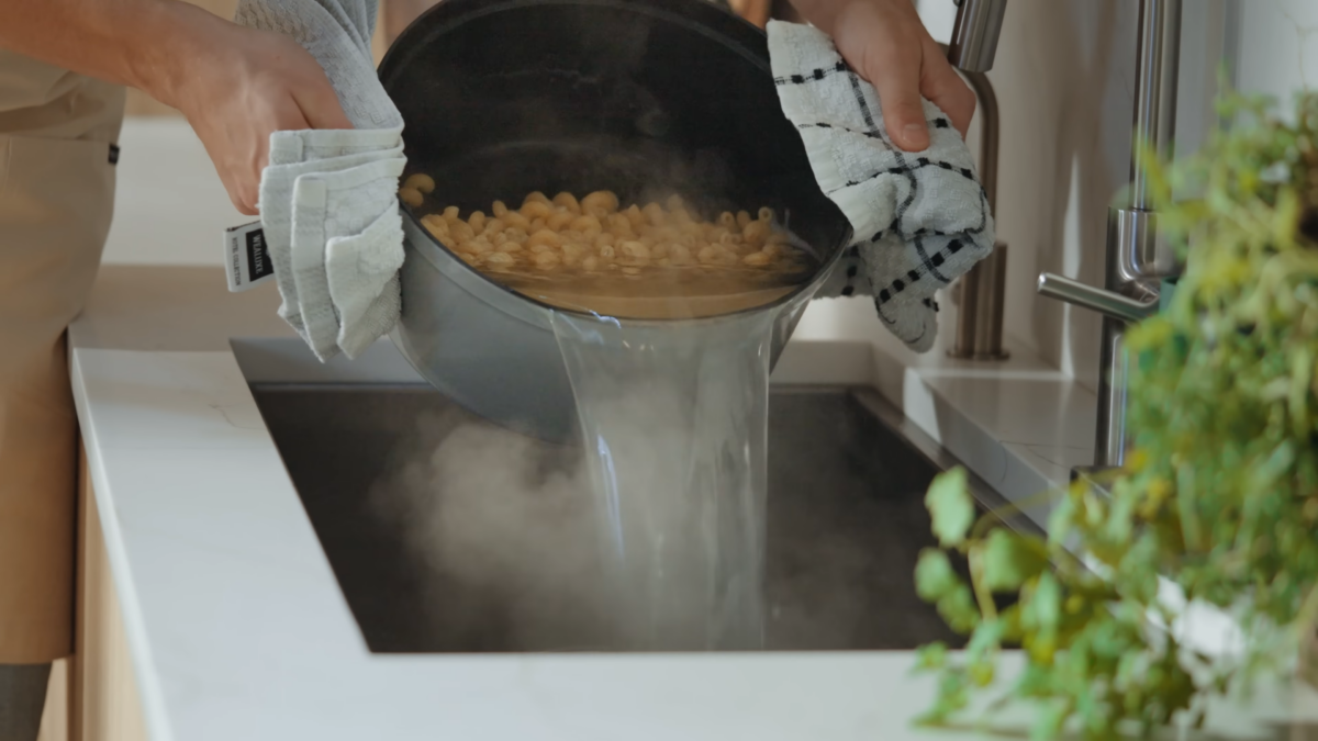 A man draining a pot of noodles over a sink.