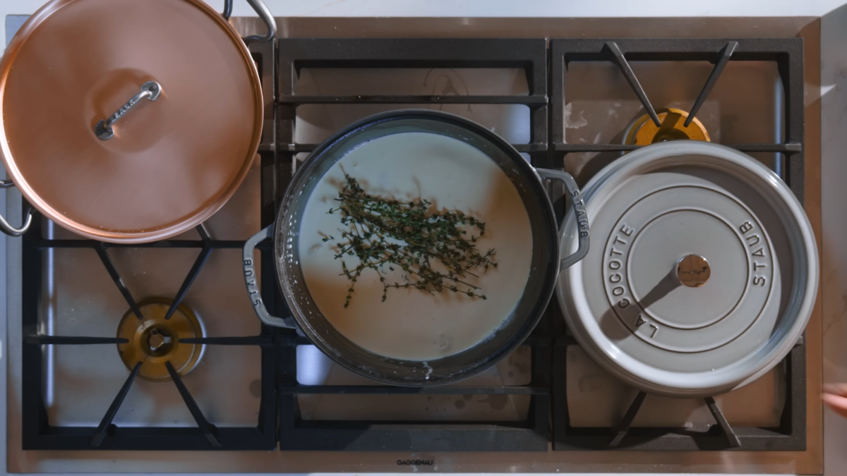 A pot of milk, cream, and fresh thyme on a stove.