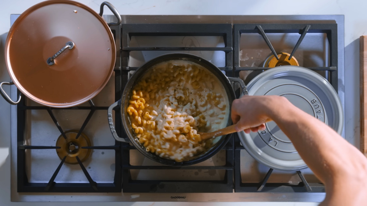A male chef mixing a pot of homemade mac and cheese.