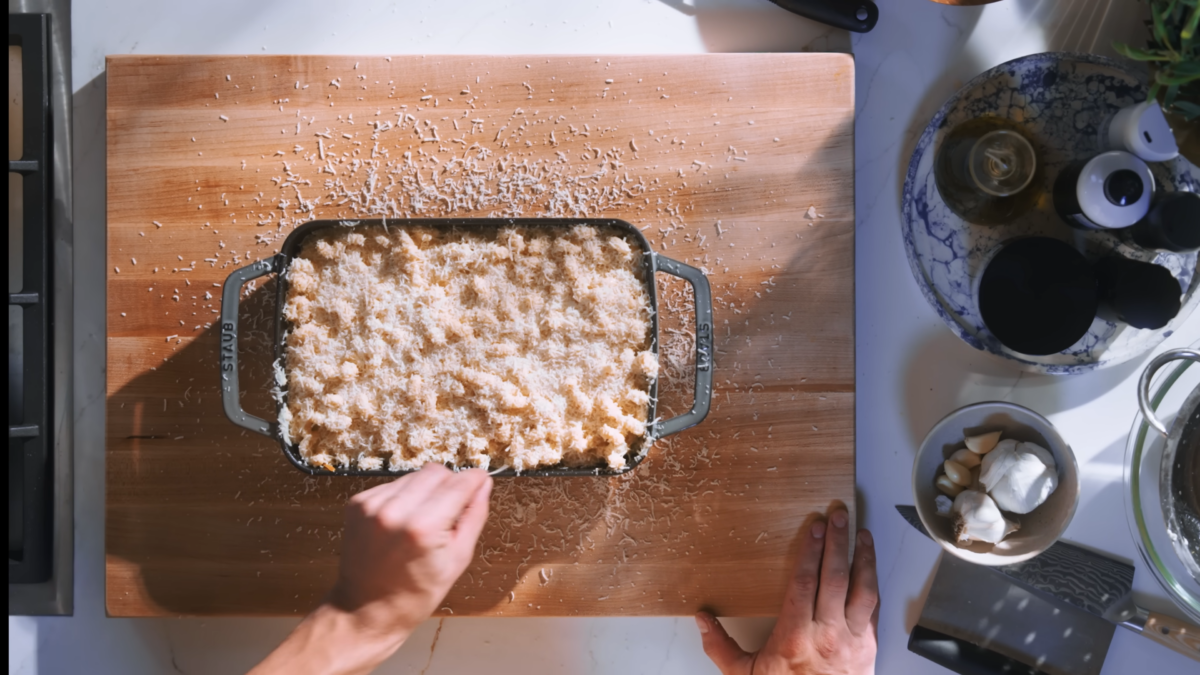 A pan of mac and cheese topped with grated parmesan cheese on a cutting board.