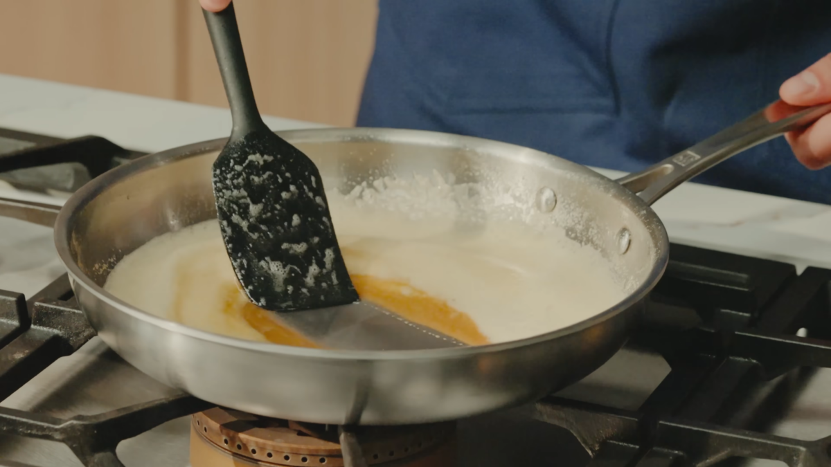 A chef mixing melted butter in a stainless steel pan.