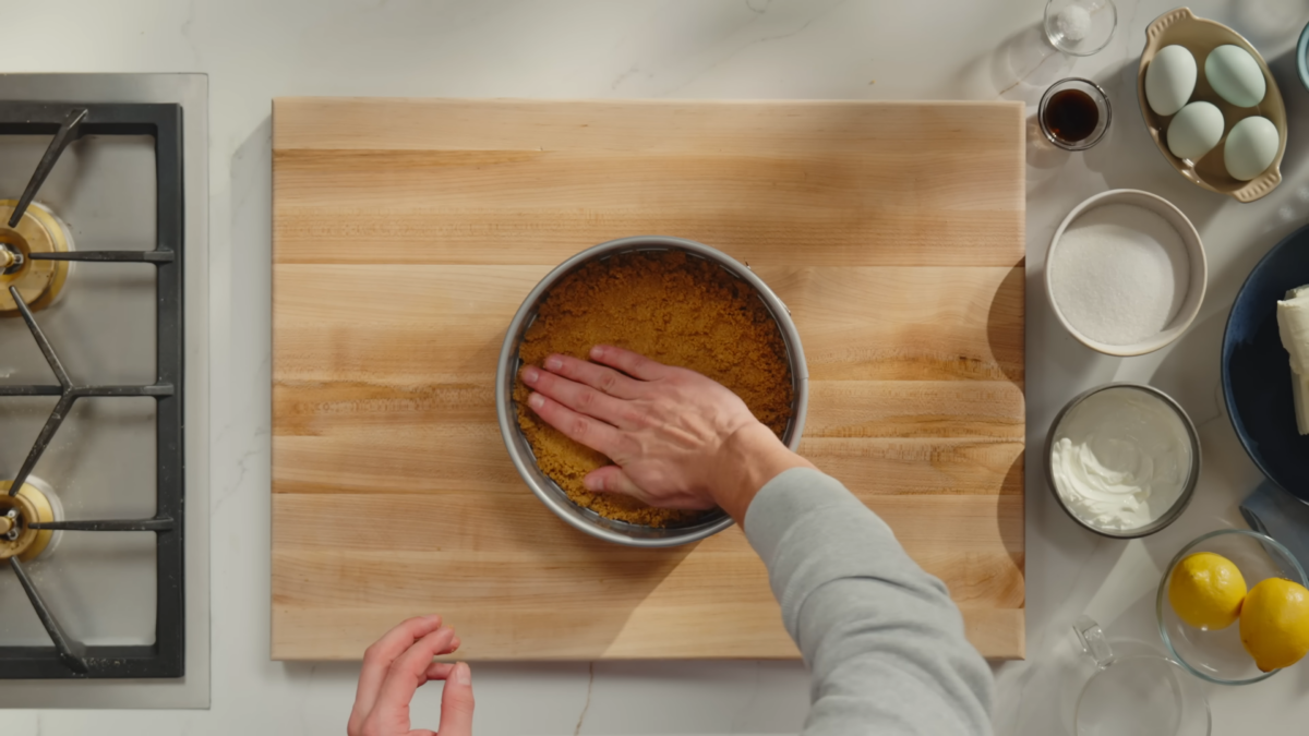 A man forming graham cracker crust to the bottom of a baking pan.