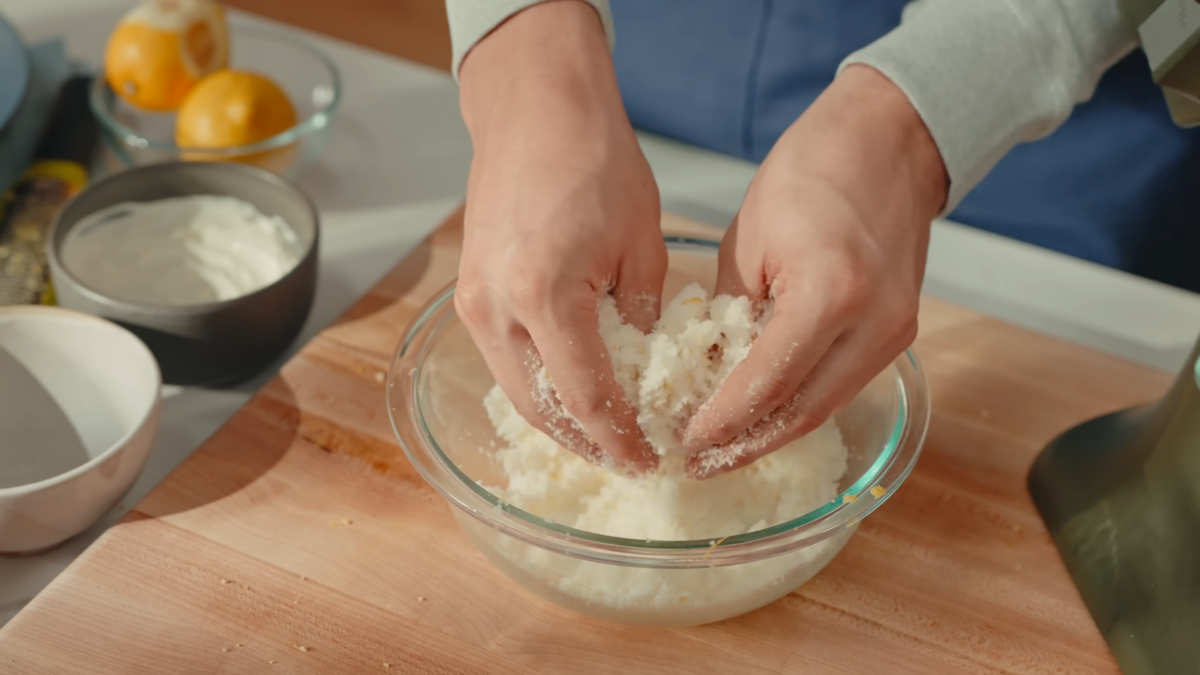 A man mixing sugar and lemon zest by hand in a glass mixing bowl.