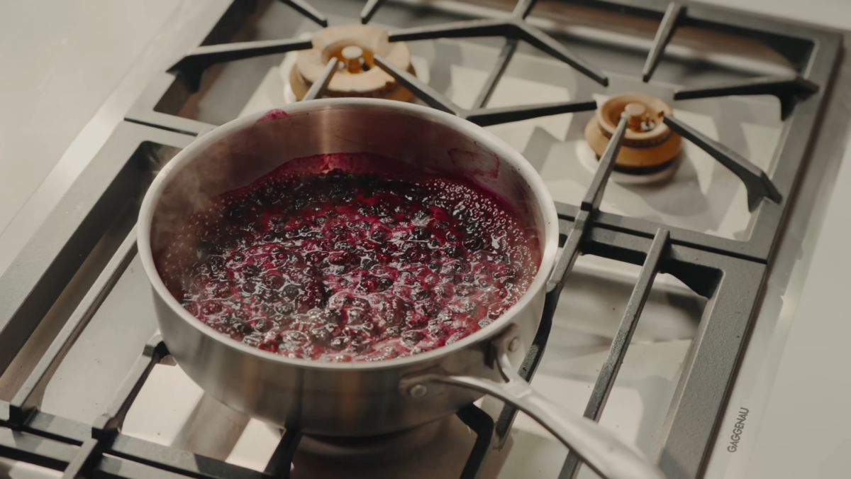 A stainless steel pan of bubbling blueberry sauce.