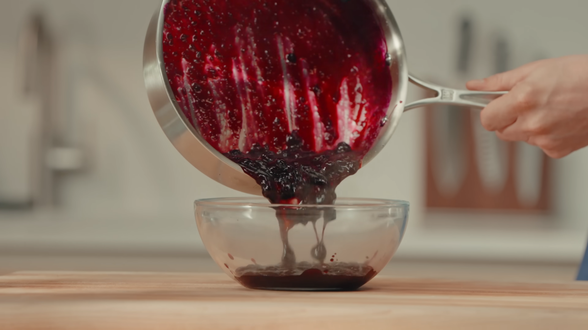 Blueberry sauce being poured into a glass mixing bowl.