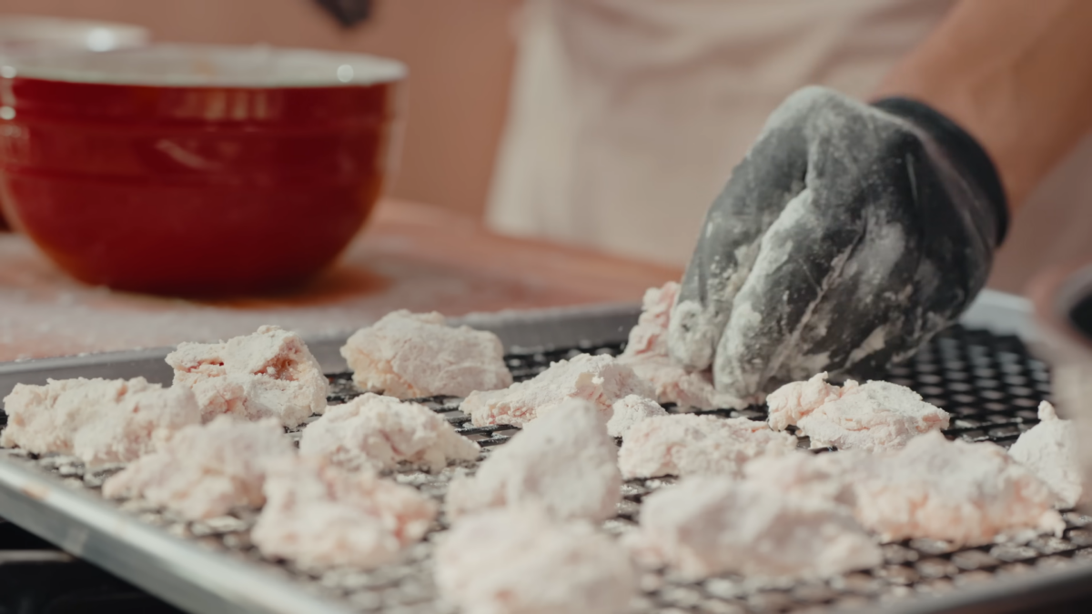 A male chef breading chicken and placing the pieces on a wire rack.