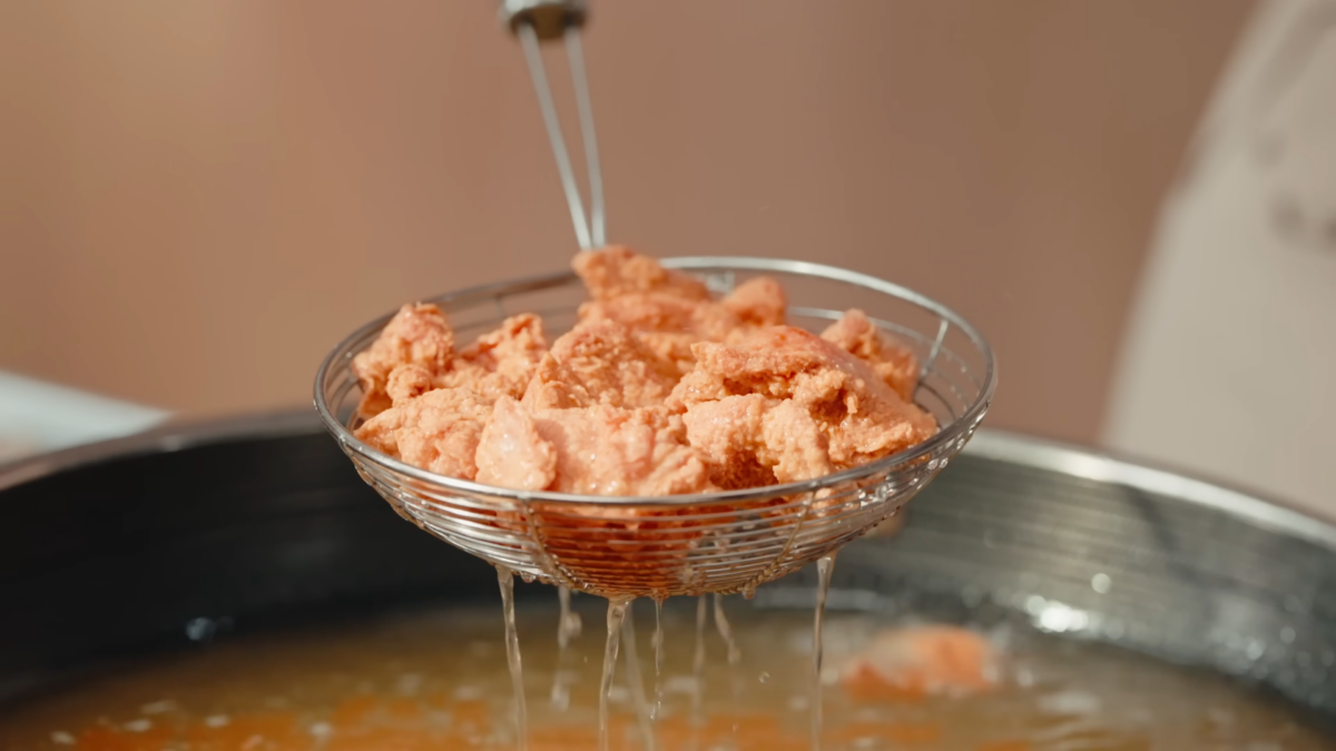 A slotted spoon holding freshly fried chicken dripping oil.
