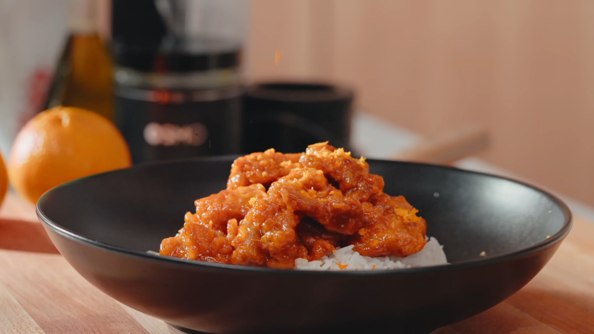 Orange chicken served over a bed of rice in a black bowl.