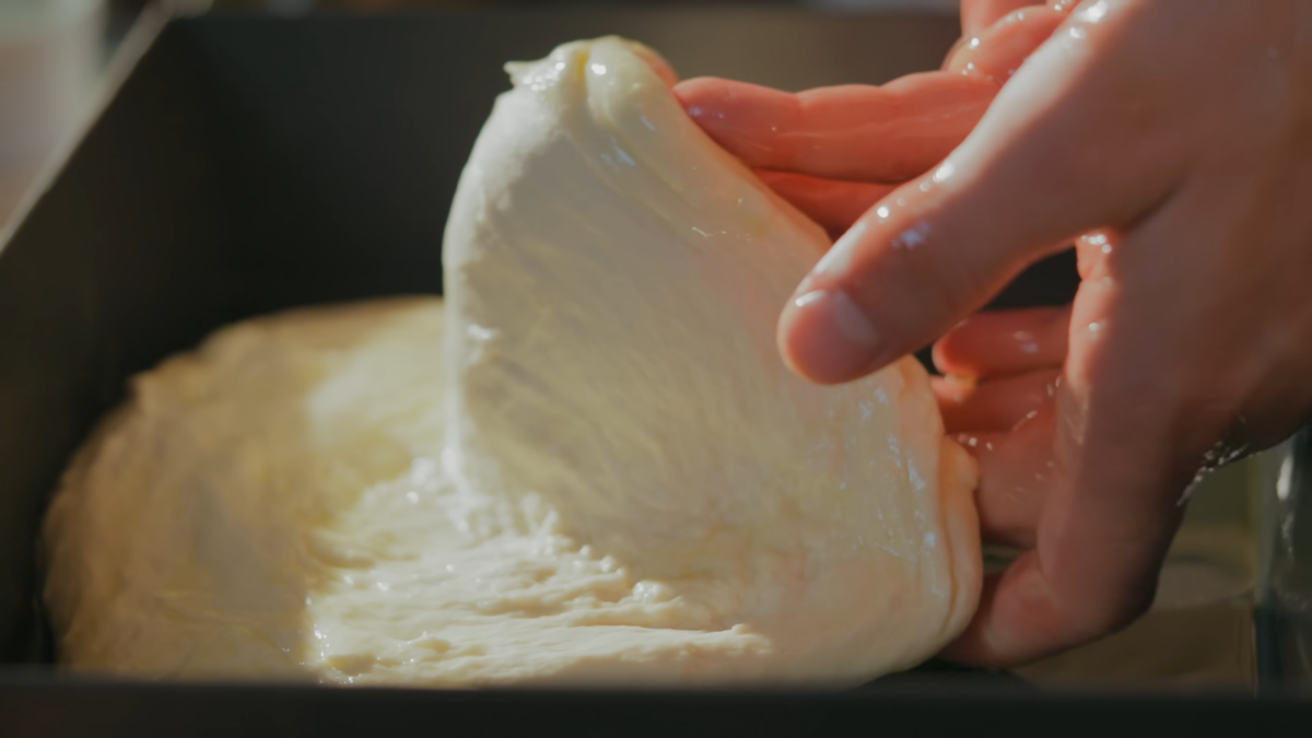 Pizza dough being stretched out in a pan.