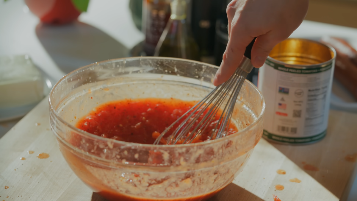A man whisking pizza sauce in a glass bowl.