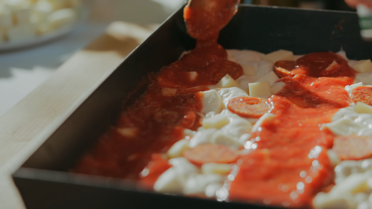 Pizza sauce being drizzled on raw pizza dough.