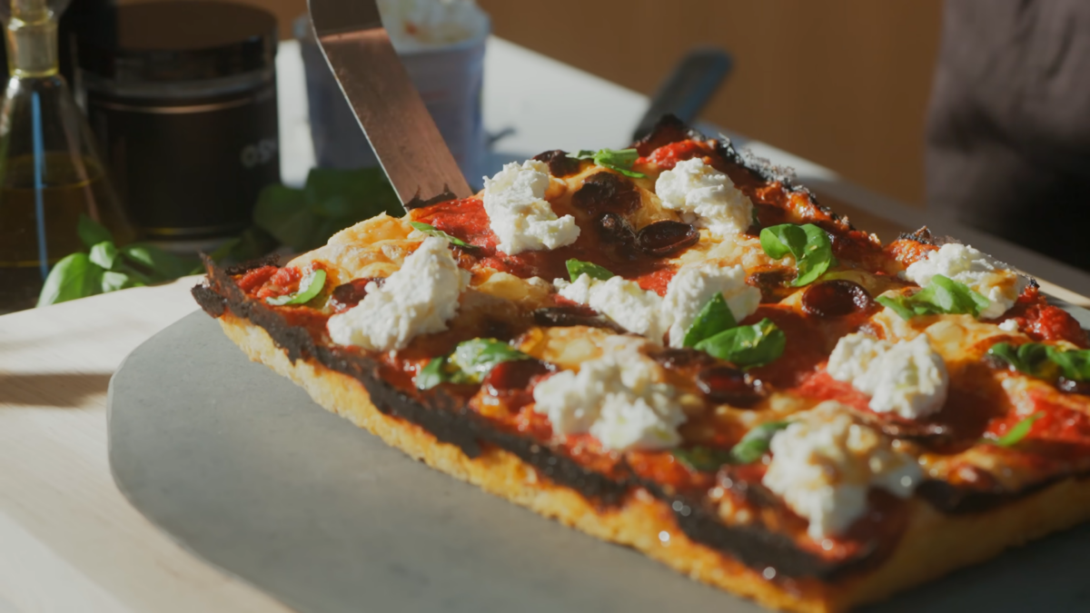 A sheet pan pizza on a cutting board topped with fresh basil and ricotta cheese.