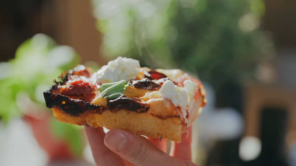 A square slice of sheet pan pizza topped with ricotta cheese and basil.
