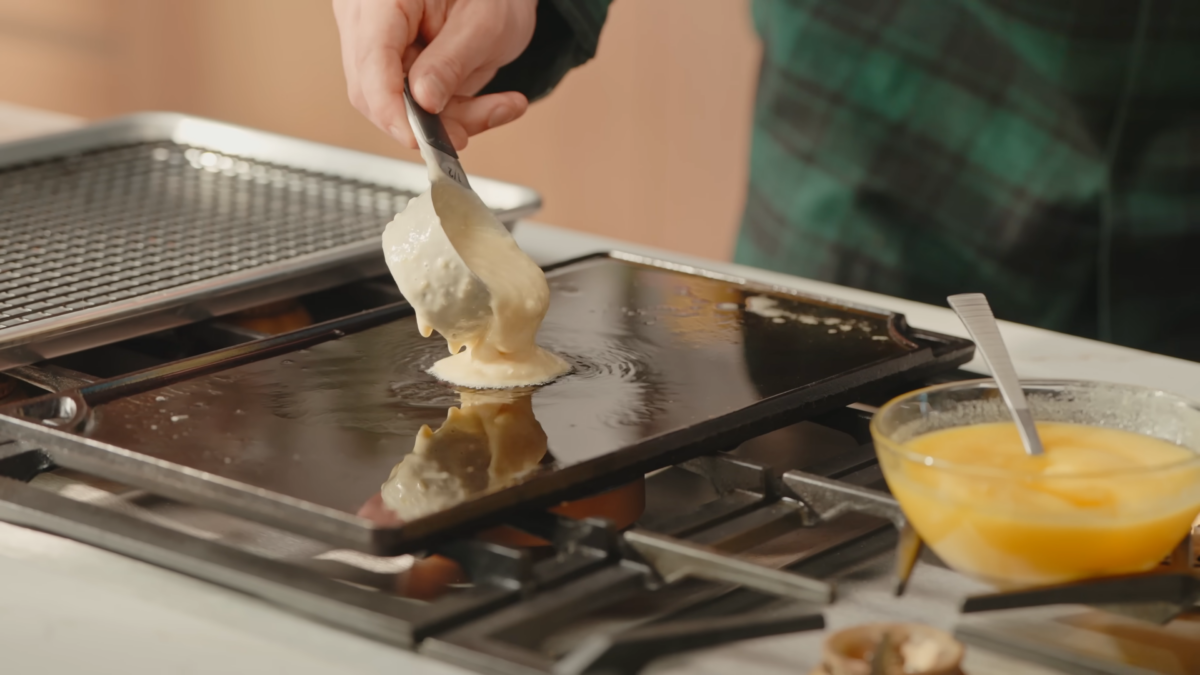 A man pouring pancake batter onto a cast iron griddle.