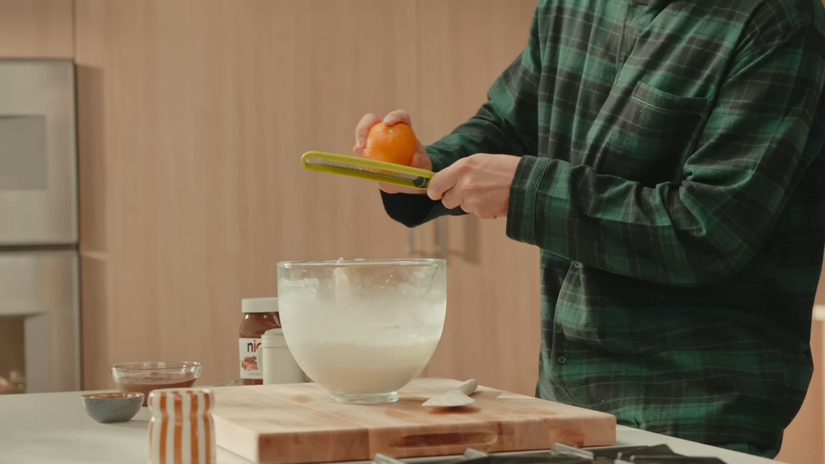 An orange being zested into a bowl of whipped cream.