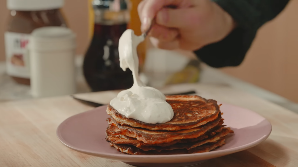 Vanilla bean whipped cream being dolloped over pancakes.