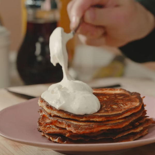 Vanilla bean whipped cream being dolloped over pancakes.