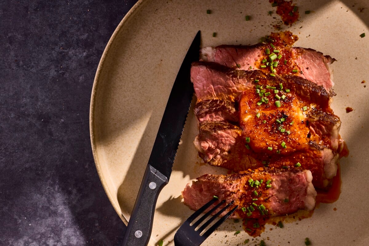 Slices of steak on a plate topped with butter and herbs.