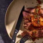 Slices of steak on a plate topped with butter and herbs.