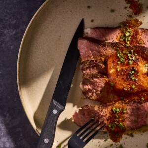 Slices of steak on a plate topped with butter and herbs.