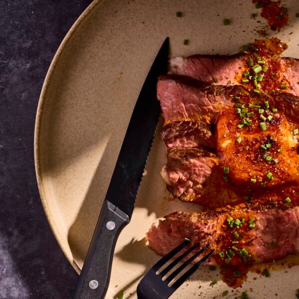 Slices of steak on a plate topped with butter and herbs.