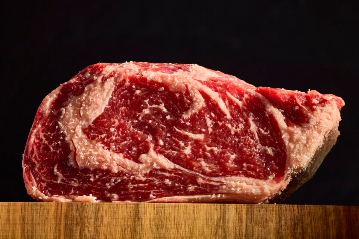 A raw ribeye steak on a wooden cutting board.