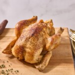 A rotisserie style whole roasted chicken on a cutting board.