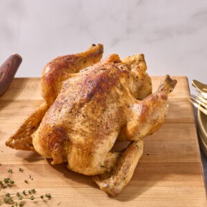 A rotisserie style whole roasted chicken on a cutting board.