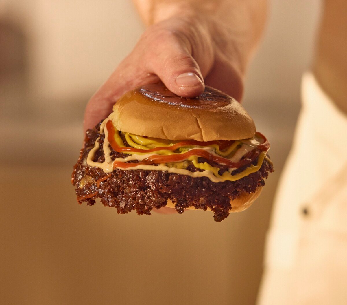 A male hand holding a Smashburger with ketchup, mustard, and burger sauce.