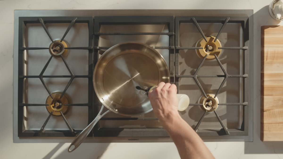 A man pouring cooking oil into a stainless steel pan.