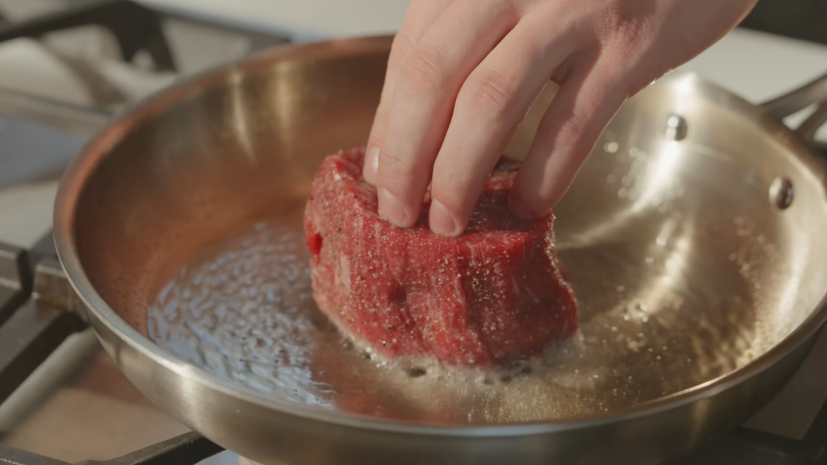 Pressing down on a steak searing in a pan.