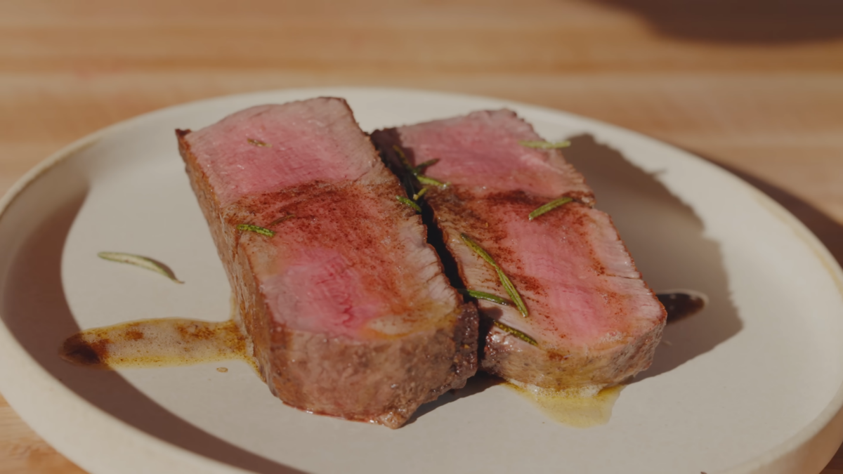 Two pieces of cut steak on a plate topped with butter and herbs.