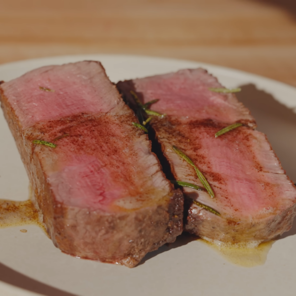 Two pieces of cut steak on a plate topped with butter and herbs.
