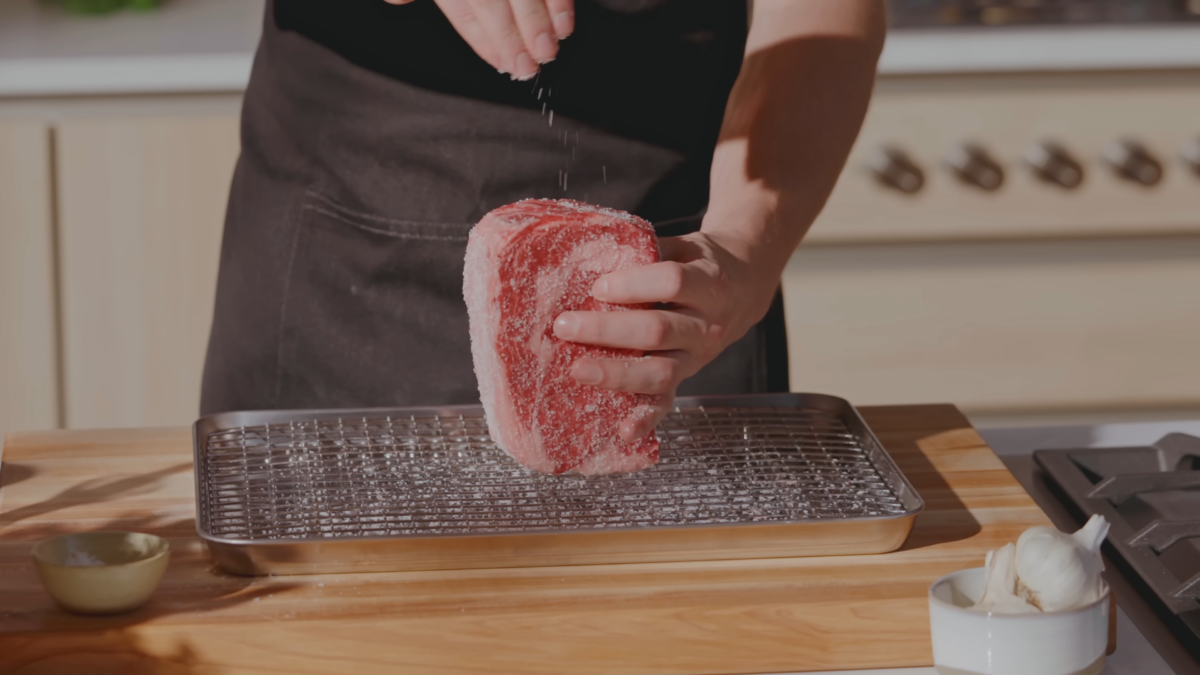 A male chef sprinkling salt on the edges of a raw steak.