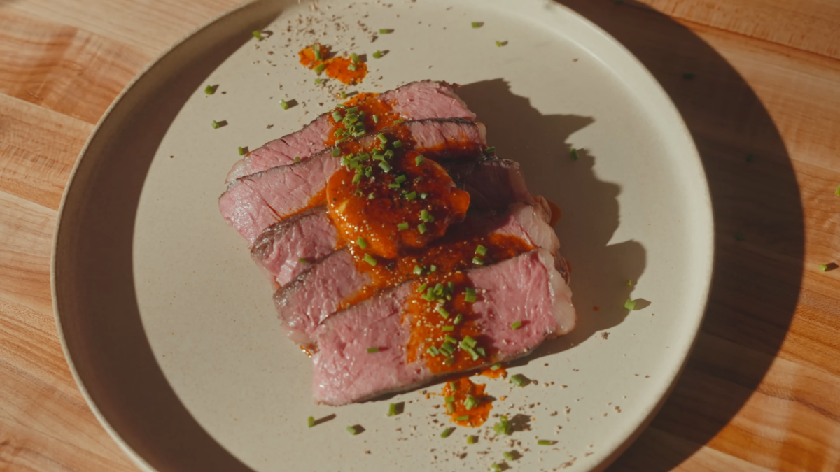 Slices of steak on a plate topped with butter and spices.