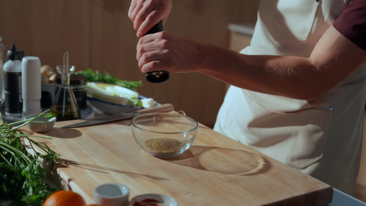 A man grinding pepper into a glass bowl of spices.