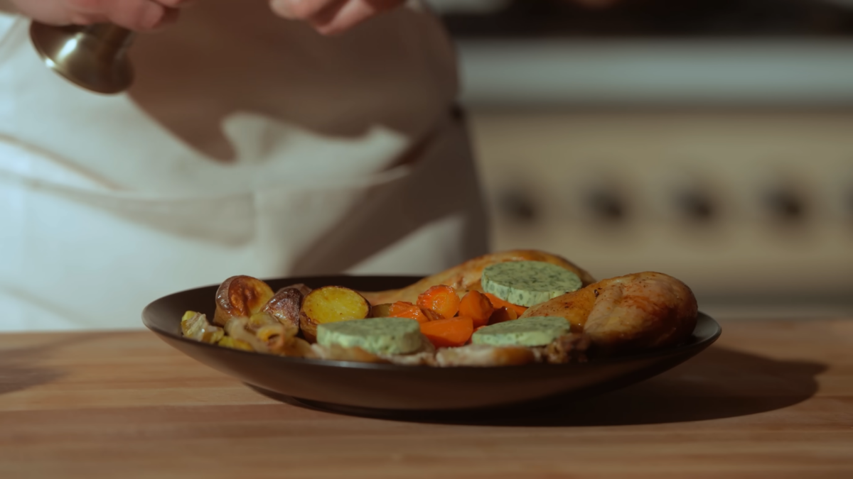 Pieces of chicken, veggies, and compound butter served on a plate.